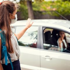 masked student waving to parent in car