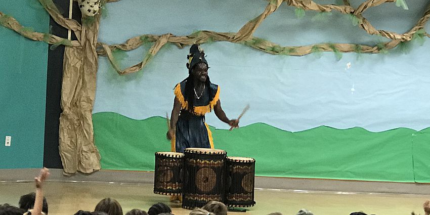 Man dressed in traditional African dress beating a drum