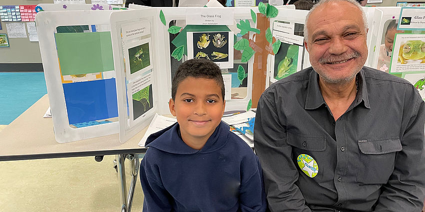 boy sits with his grandfather in front of a school display about frogs