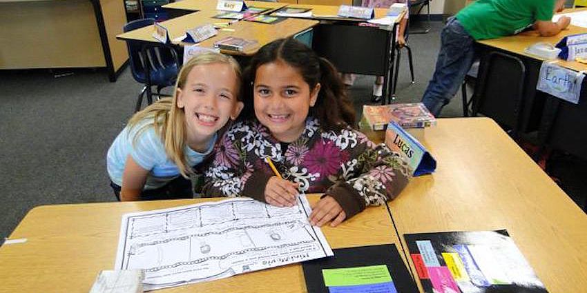 two smiling girls working on classwork
