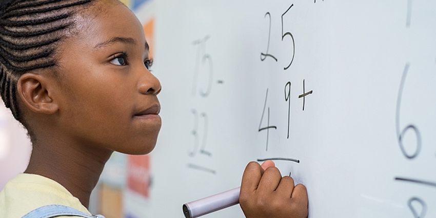 young girl working a math problem on a white board