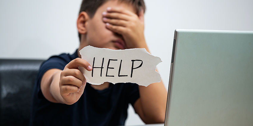 Student at a computer holding up a help sign
