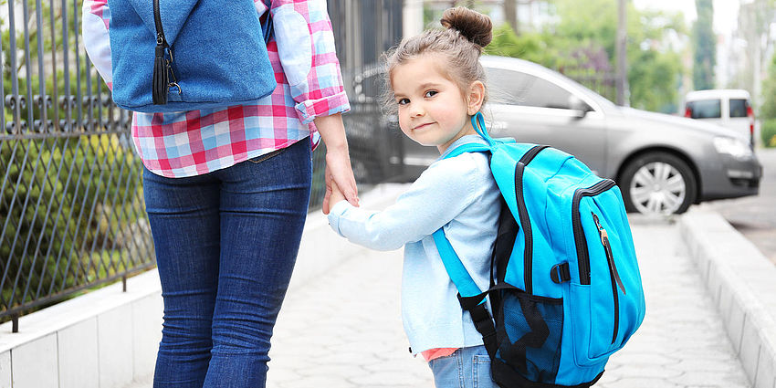 girl with backpack walking to school with parent