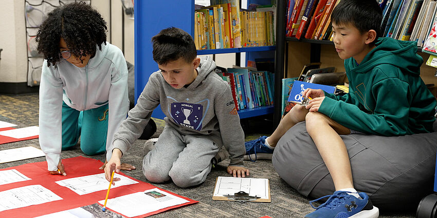 one girl and two boys sit on floor discussing the documents laying before them