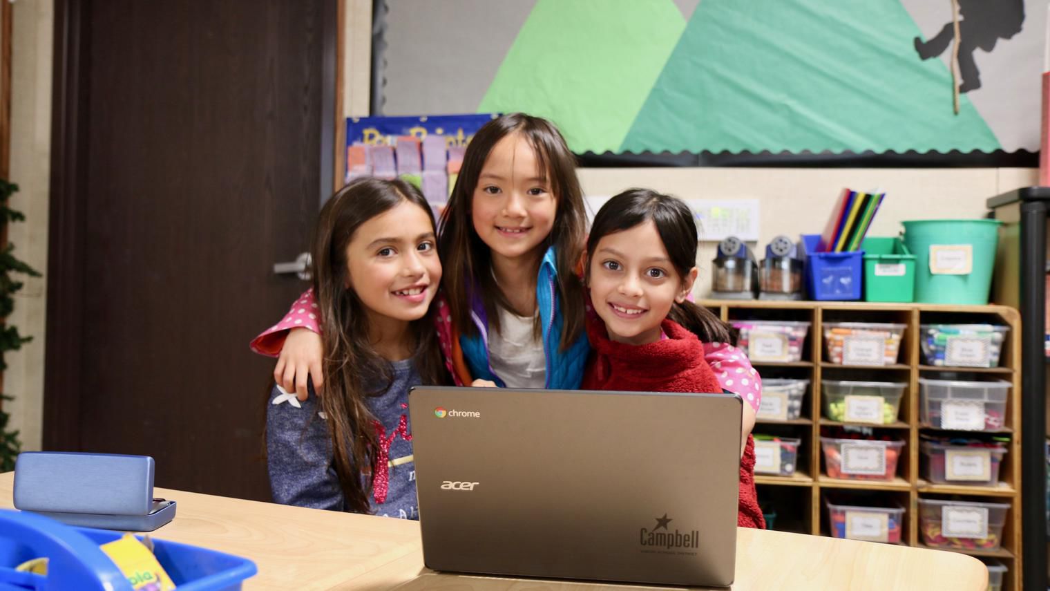 three girls hugging in front of a chromebook