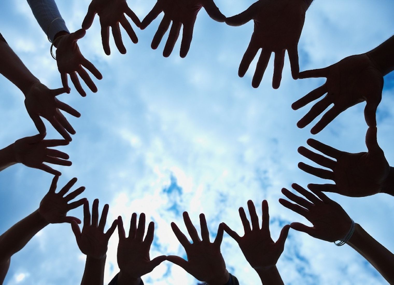 Group of hands with the sky as the background.