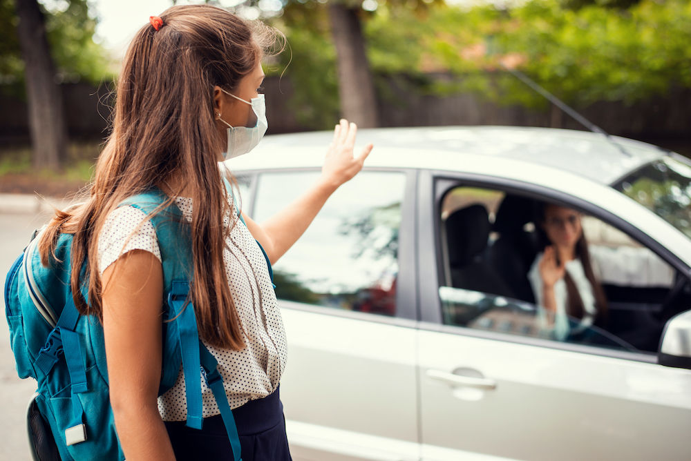 Student waving goodbye to parent in car.