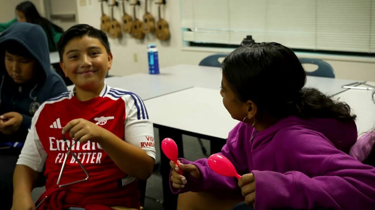 boy smiling and holding a triangle musical instrument.